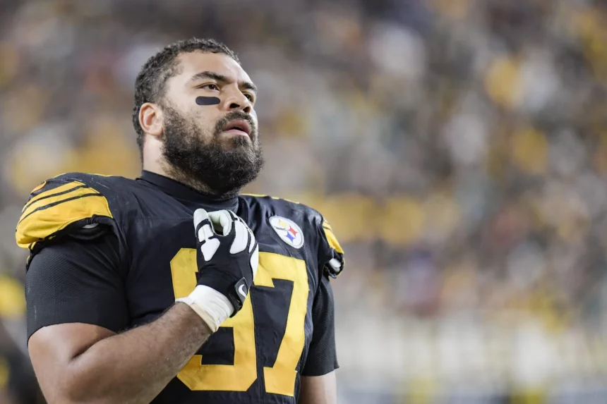 Cam Heyward, über 30 und mit der Nummer 97 im schwarz-gelben Steelers-Trikot, steht mit der Hand auf der Brust auf dem Spielfeld und blickt nach oben, während die Menschenmenge im Stadionhintergrund verschwimmt. Diese Beschreibung wurde mit der FootballR KI automatisch generiert.