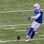 Kicker der Colts versucht einen Onside Kick - rechtes Bein ist ausgestreckt, während der Ball in der Luft über die weißen Yard-Linien und ein schwarzes Kicking-Tee auf dem Rasen fliegt. Diese Beschreibung wurde mit der FootballR KI automatisch generiert.