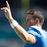 Ein Footballspieler in einem blauen Trikot mit weißen und gelben Details hebt seine rechte Hand und zeigt mit zwei Fingern nach oben. Mit "RIVERS" und der Nummer "17" auf seinem Trikot gestikuliert Philip Rivers jubelnd, bevor er seine Karriere beendet. Diese Beschreibung wurde mit der FootballR KI automatisch generiert.