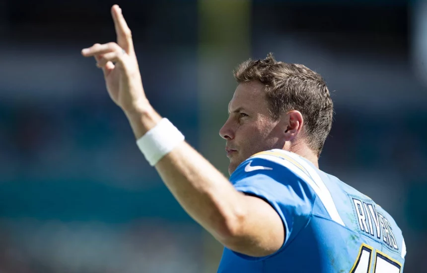 Ein Footballspieler in einem blauen Trikot mit weißen und gelben Details hebt seine rechte Hand und zeigt mit zwei Fingern nach oben. Mit "RIVERS" und der Nummer "17" auf seinem Trikot gestikuliert Philip Rivers jubelnd, bevor er seine Karriere beendet. Diese Beschreibung wurde mit der FootballR KI automatisch generiert.