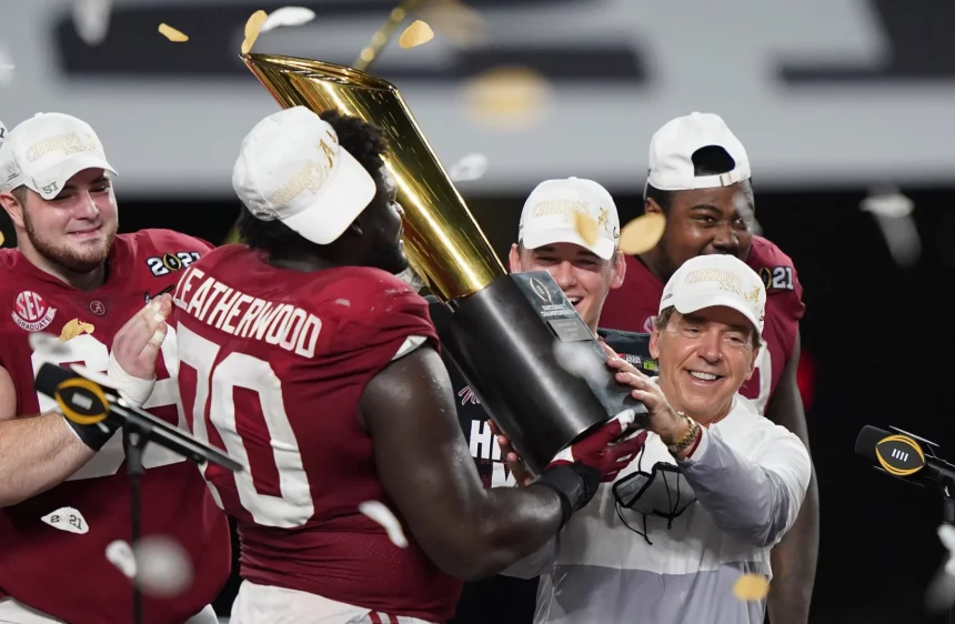 Kalen DeBoer will mit Alabama zurück an die Spitze. Eine Footballmannschaft in roten Trikots feiert den Gewinn der Nationalmeisterschaft. Die Spieler tragen weiße Hüte und halten einen großen goldenen Pokal in den Händen, während Konfetti um sie herum regnet. Ein Mann in weißer Jacke hilft, den Pokal zu halten, und lächelt zwischen den Spielern auf einer Bühne mit schwarz-weißem Hintergrund. Diese Beschreibung wurde mit der FootballR KI automatisch generiert.