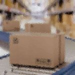 Ein Karton bewegt sich auf einem Förderband in einem Lagerhaus mit hohen Regalen, die mit ähnlichen Kartons gefüllt sind. Der Hintergrund erscheint unscharf, wodurch der Karton im Vordergrund hervorgehoben wird. Die Kulisse lässt auf ein geschäftiges Logistik- oder Vertriebszentrum schließen. Diese Beschreibung wurde mit der FootballR KI automatisch generiert.