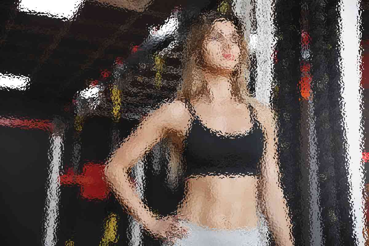 Eine Frau in Trainingskleidung steht selbstbewusst in einem Fitnessstudio. Sie trägt einen schwarzen Sport-BH und helle Hosen. Ihr langes Haar ist offen und ihre Hände ruhen auf ihren Hüften. Der Hintergrund des Fitnessstudios besteht aus Trainingsgeräten und dezenter Beleuchtung, wodurch eine konzentrierte und zielstrebige Atmosphäre entsteht. Diese Beschreibung wurde mit der FootballR KI automatisch generiert.