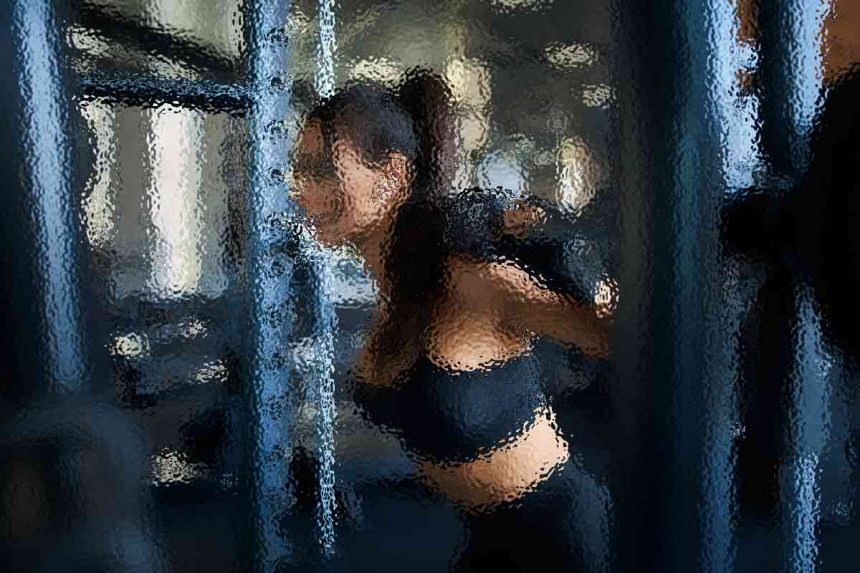 Eine Person mit langen Haaren trainiert in einem Fitnessstudio und macht Kniebeugen mit einer Hantel auf den Schultern. Sie trägt ein dunkles Sportoutfit. Der Hintergrund ist verschwommen, man sieht Fitnessgeräte und sanftes Licht, was eine konzentrierte Atmosphäre schafft. Diese Beschreibung wurde mit der FootballR KI automatisch generiert.