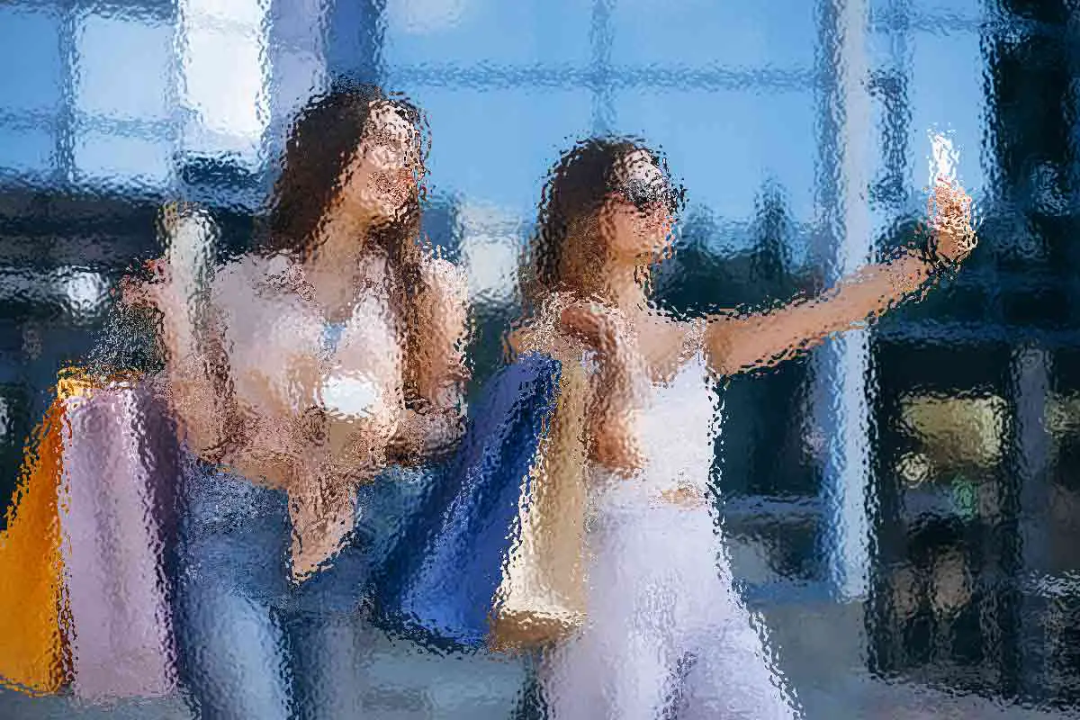 Zwei Frauen stehen vor einem Gebäude mit Glasfenstern und halten Einkaufstüten. Eine trägt eine helle Bluse und Jeans und trägt Kaffee und Tüten. Die andere in einem weißen Oberteil und rosafarbenen Hosen macht ein Selfie, trägt eine Sonnenbrille und hält Tüten. Das Bild hat einen malerischen Effekt mit leuchtenden Farben. Diese Beschreibung wurde mit der FootballR KI automatisch generiert.