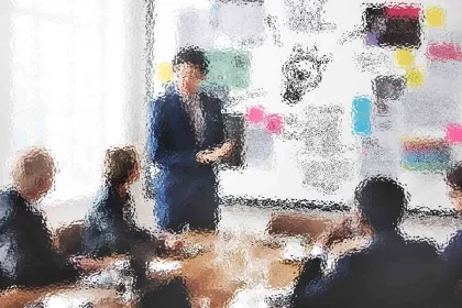 Ein verschwommenes Bild eines Leiters bei einem Geschäftstreffen. Die Person steht neben einer großen Tafel voller bunter Notizen und Diagramme und präsentiert vier sitzenden Kollegen etwas. Der Raum ist gut beleuchtet, da natürliches Licht durch ein großes Fenster fällt. Diese Beschreibung wurde mit der FootballR KI automatisch generiert.