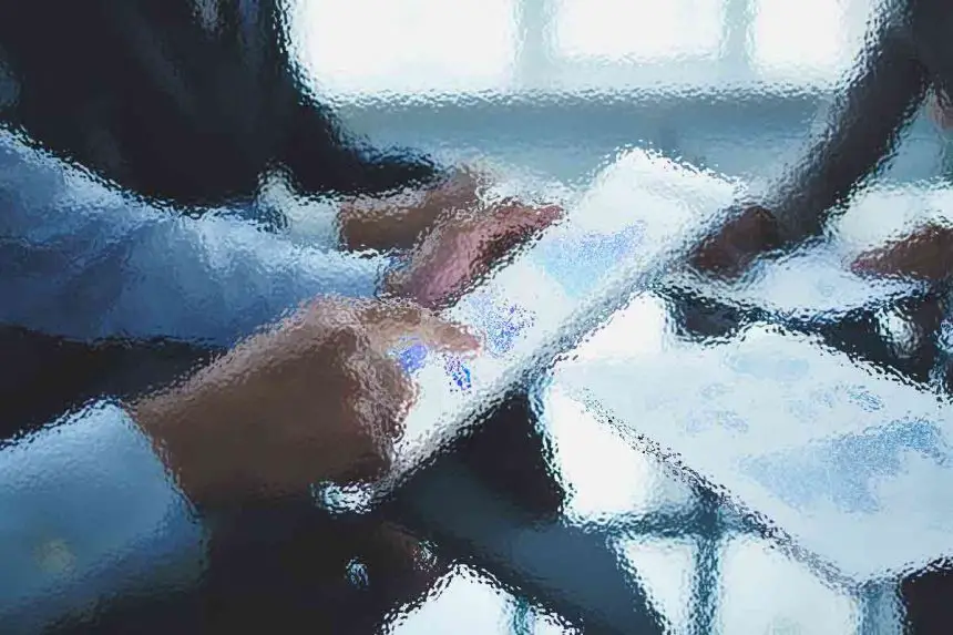 Unscharfes Bild von Menschen in einem Besprechungsraum, mit Fokus auf die Hände. Eine Hand hält ein Tablet mit einem Diagramm. Auf einem reflektierenden Tisch liegen verstreut Dokumente. Die Umgebung lässt auf eine Geschäftsumgebung mit Personen in formeller Kleidung schließen. Sanftes Licht kommt von einem Fenster im Hintergrund. Diese Beschreibung wurde mit der FootballR KI automatisch generiert.