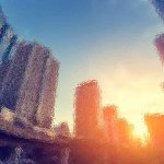 Abstrakte Stadtlandschaft bei Sonnenuntergang mit verschwommenen, verzerrten Wolkenkratzern. Die Sonne geht am Horizont unter und wirft einen orangefarbenen Schimmer auf die Gebäude. Der Himmel wechselt von Blau zu einem warmen Gelb und Orange und schafft so eine verträumte, surreale Atmosphäre. Diese Beschreibung wurde mit der FootballR KI automatisch generiert.