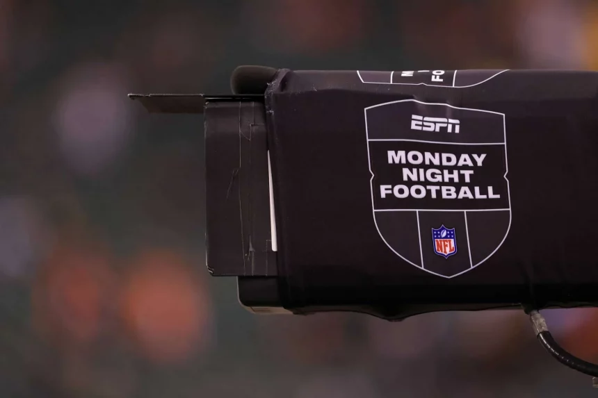 ESPN kauft NFL Network - NFL-Quoten - Nahaufnahme einer Fernsehkamera, die mit einer schwarzen Hülle bedeckt ist, auf der das ESPN-Logo und der Text "Monday Night Football" zusammen mit dem NFL-Schild abgebildet sind, um die Rechte von ESPN zur Übertragung des Monday Night Wild Card Game hervorzuheben; unscharfer Stadionhintergrund. Diese Beschreibung wurde mit der FootballR KI automatisch generiert.