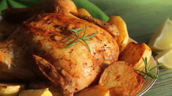 Roasted whole chicken with rosemary served with potatoes on wooden table, dinner, christmas background