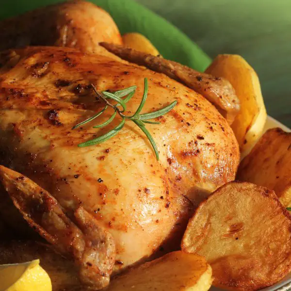 Roasted whole chicken with rosemary served with potatoes on wooden table, dinner, christmas background