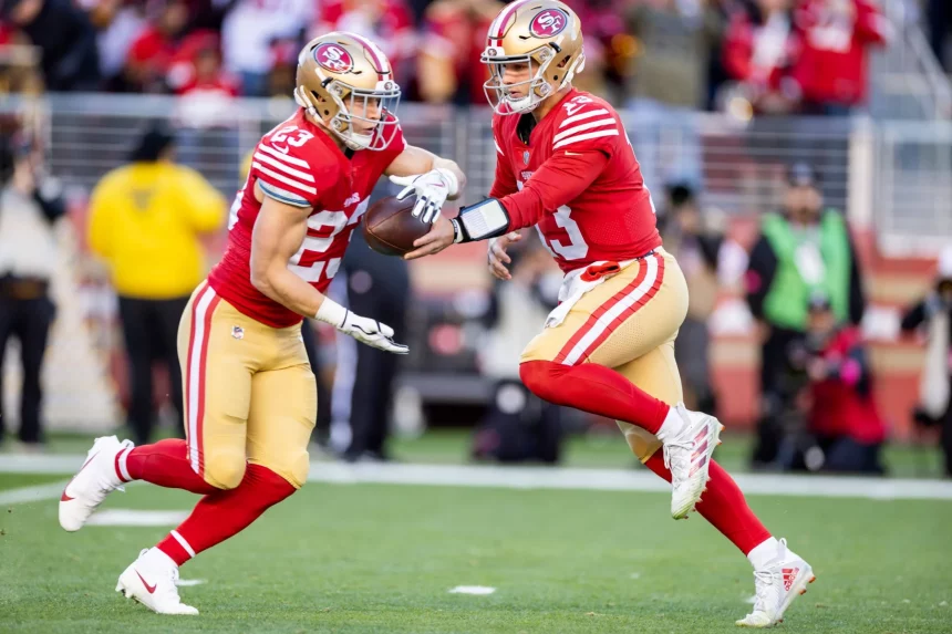 FootballR - NFL - RTL NFL Woche 15 - Zwei Spieler der San Francisco 49ers, Brock Purdy und Christian McCaffrey, laufen mit dem Ball.