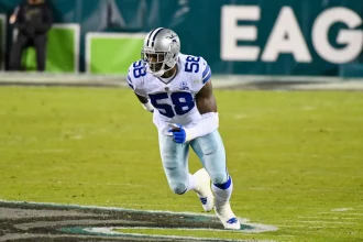 Der Footballspieler der Dallas Cowboys, Aldon Smith, mit der Rückennummer 58, rennt während eines Spiels über das Spielfeld, wobei im Hintergrund ein Teil des Wortes „EAGLES“ zu sehen ist. Alt-Text wurde KI-generiert.
