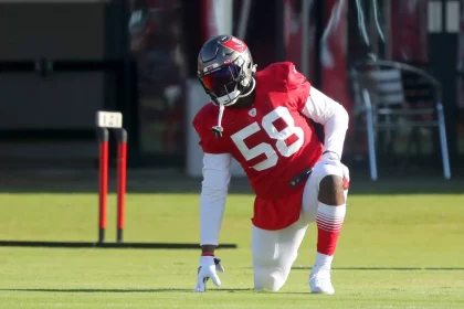 Shaquil Barrett auch Shaq Barrett genannt in einem roten Trikot mit der Nummer 58 und weißen Hosen kniet beim Training auf dem Rasen. Tochter Barretts typischer Stil wird durch seinen Helm mit dunklem Visier deutlich. Im Hintergrund sind Ausrüstung und Sitzgelegenheiten zu sehen. Diese Beschreibung wurde mit der FootballR KI automatisch generiert.