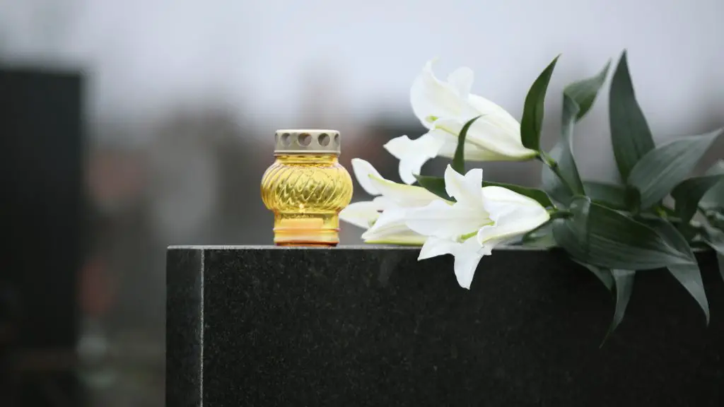 White lilies and candle on black granite tombstone outdoors. Funeral ceremony Devon Wylie