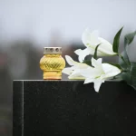 White lilies and candle on black granite tombstone outdoors. Funeral ceremony Devon Wylie