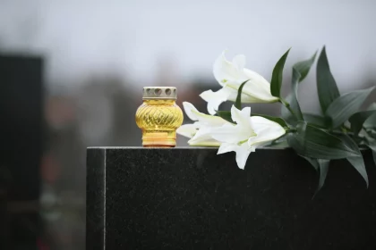 White lilies and candle on black granite tombstone outdoors. Funeral ceremony Devon Wylie