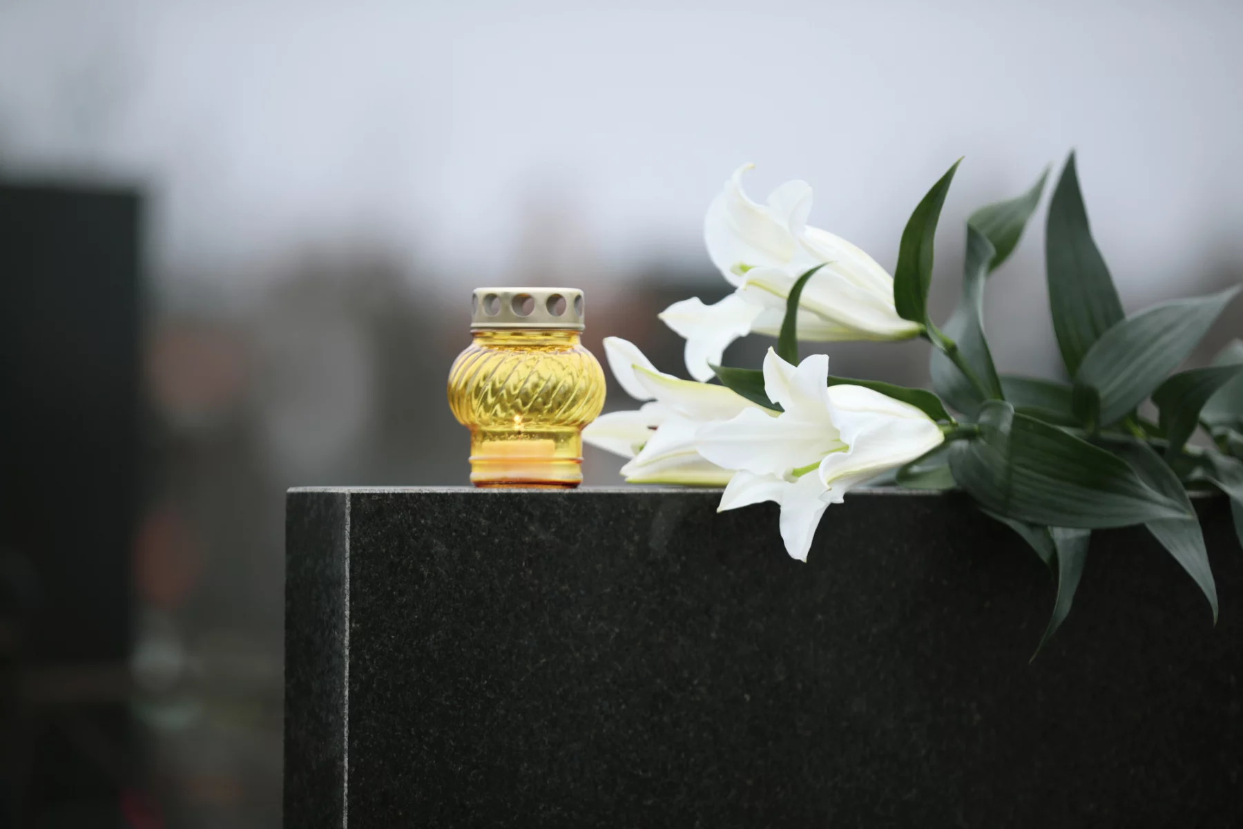 White lilies and candle on black granite tombstone outdoors. Funeral ceremony Devon Wylie