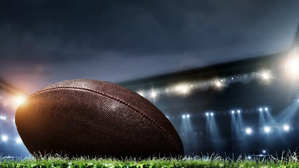 Night football arena in lights and flashes with american football ball on the foreground