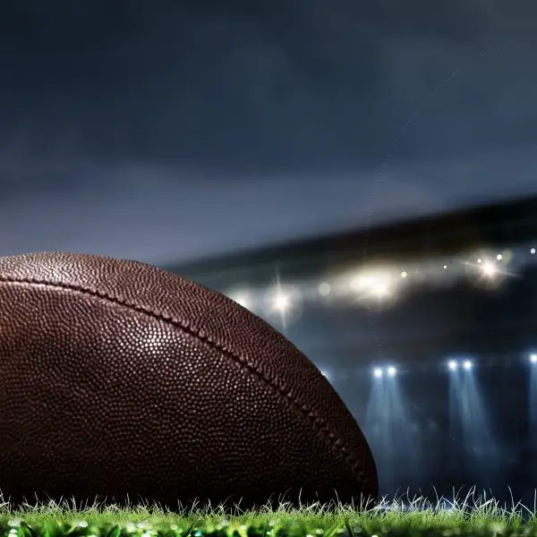 Night football arena in lights and flashes with american football ball on the foreground