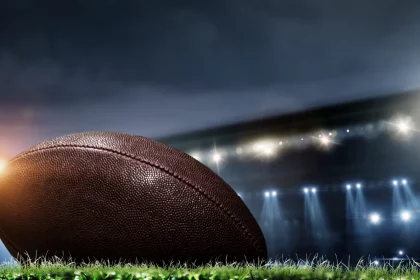 Night football arena in lights and flashes with american football ball on the foreground