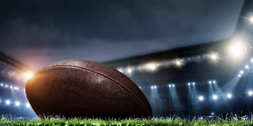 Night football arena in lights and flashes with american football ball on the foreground