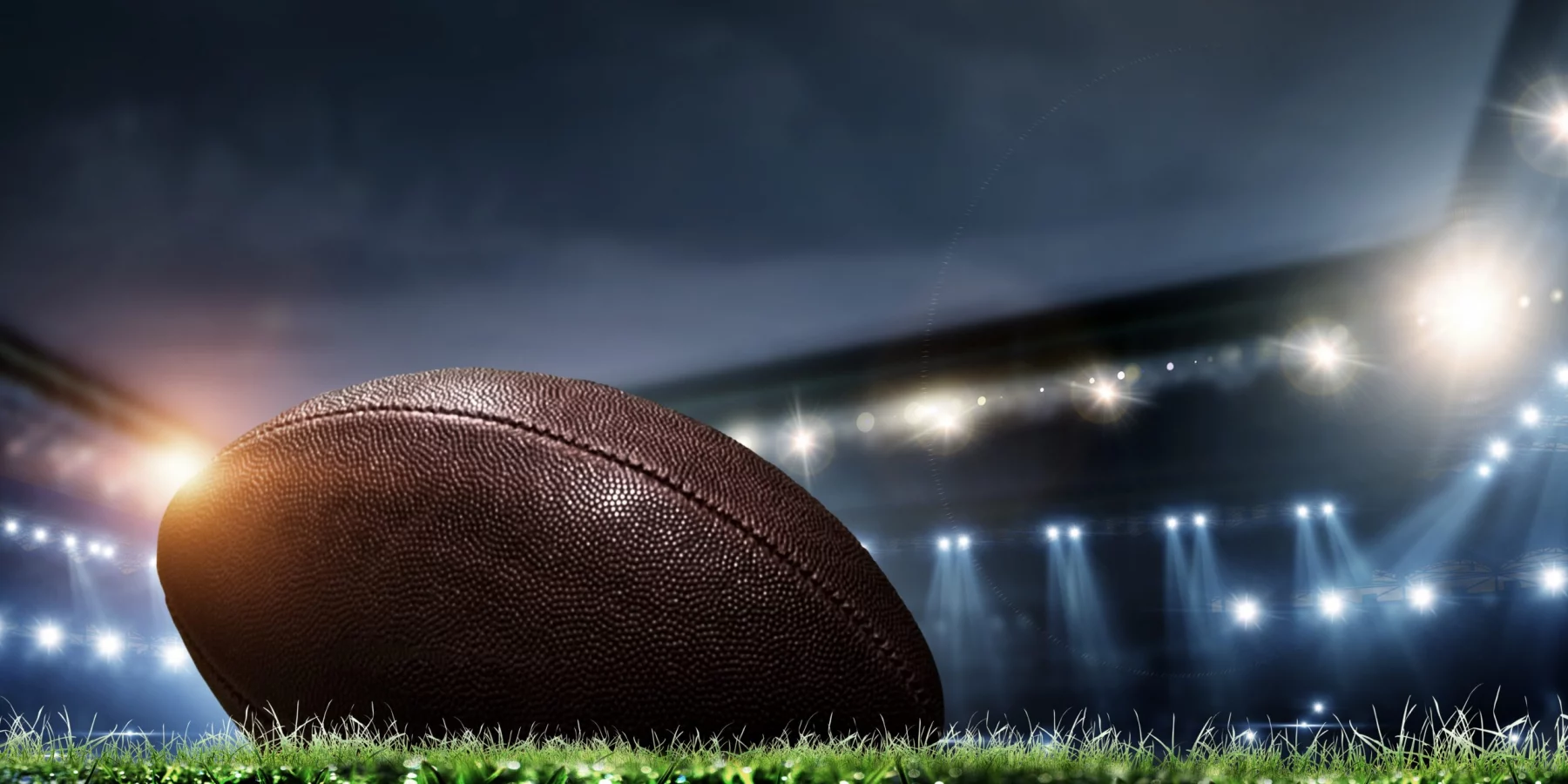 Night football arena in lights and flashes with american football ball on the foreground