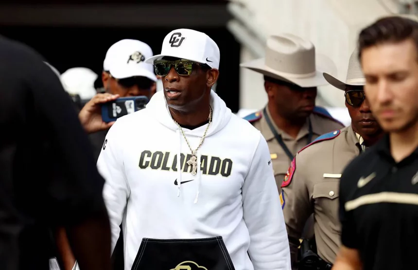 FootballR - NFL - Deion Sanders, bekleidet mit einem weißen Kapuzenpullover, navigiert durch eine Menschenmenge.