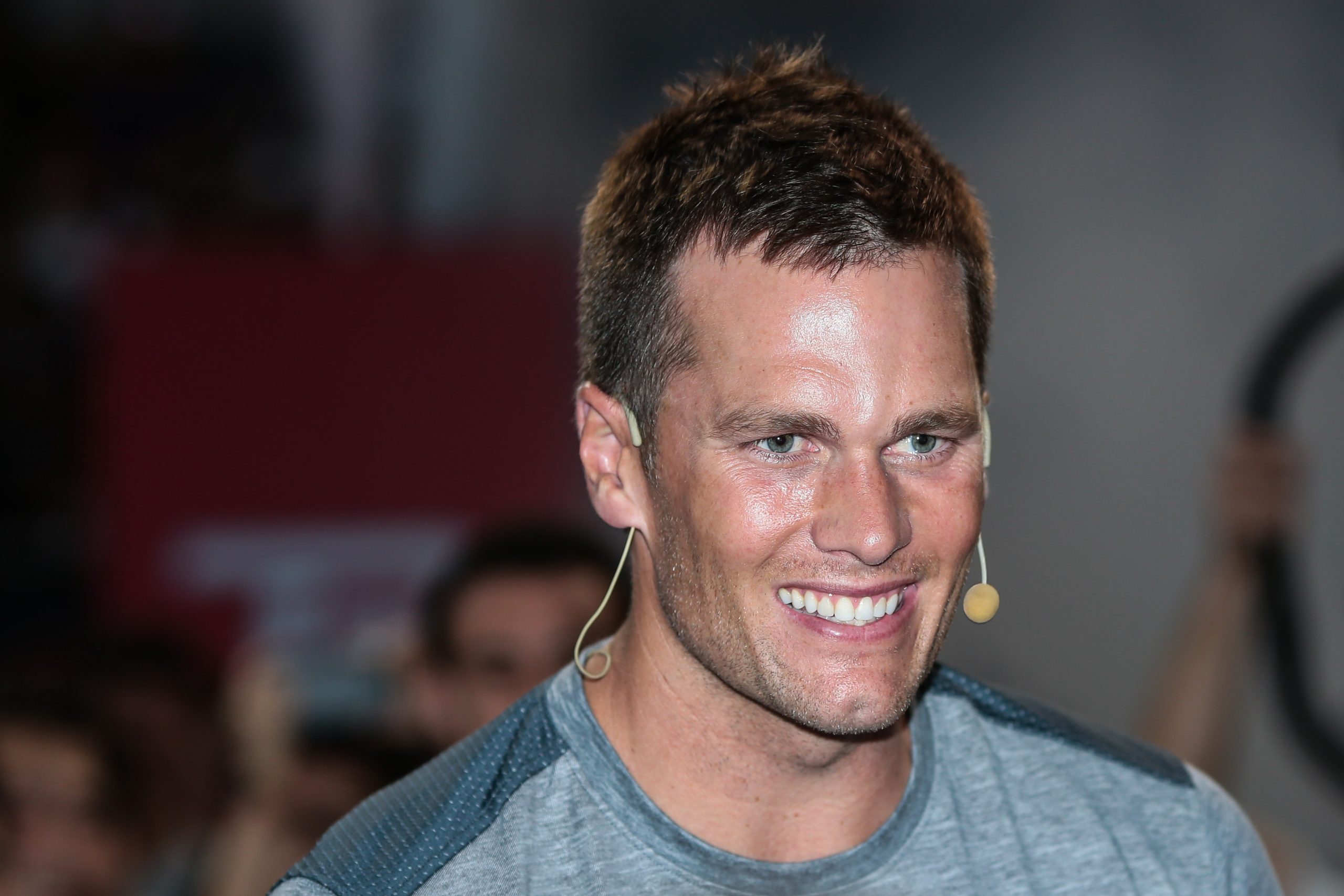 FootballR - NFL - Ein Mann, Tom Brady, lächelt vor einer Menschenmenge bei einer offiziellen Veranstaltung.