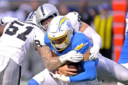 FootballR - NFL - Justin Herbert spielt mit gebrochenem Finger und wird hier im Bild von Maxx Crosby getackelt.