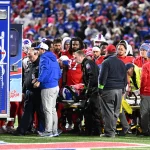 FootballR - NFL - Buffalo Bills RB Damien Harris aus dem Krankenhaus entlassen, während eine Gruppe von Menschen auf einem Footballfeld um einen Rettungswagen her