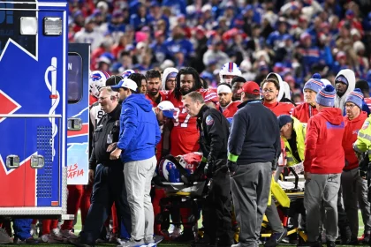 FootballR - NFL - Buffalo Bills RB Damien Harris aus dem Krankenhaus entlassen, während eine Gruppe von Menschen auf einem Footballfeld um einen Rettungswagen her