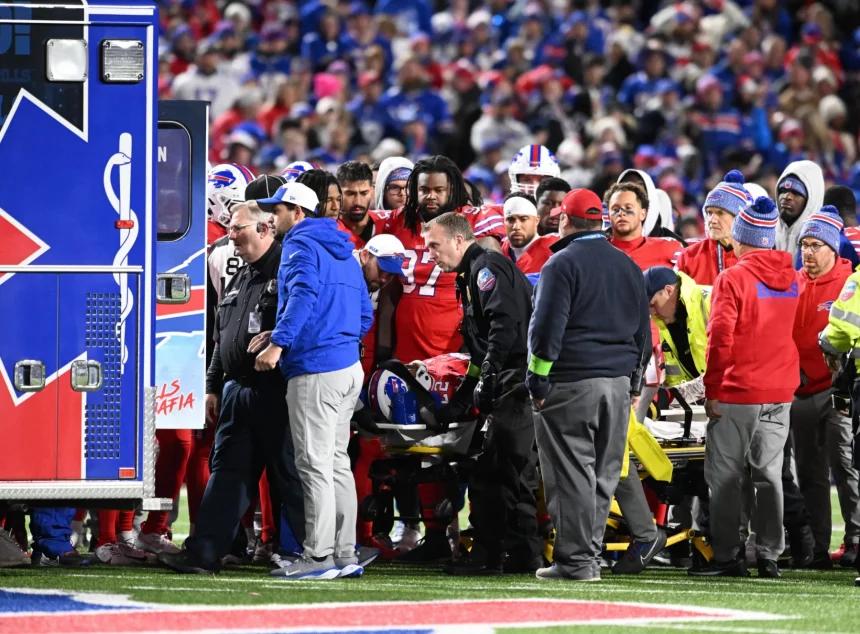 FootballR - NFL - Buffalo Bills RB Damien Harris aus dem Krankenhaus entlassen, während eine Gruppe von Menschen auf einem Footballfeld um einen Rettungswagen her