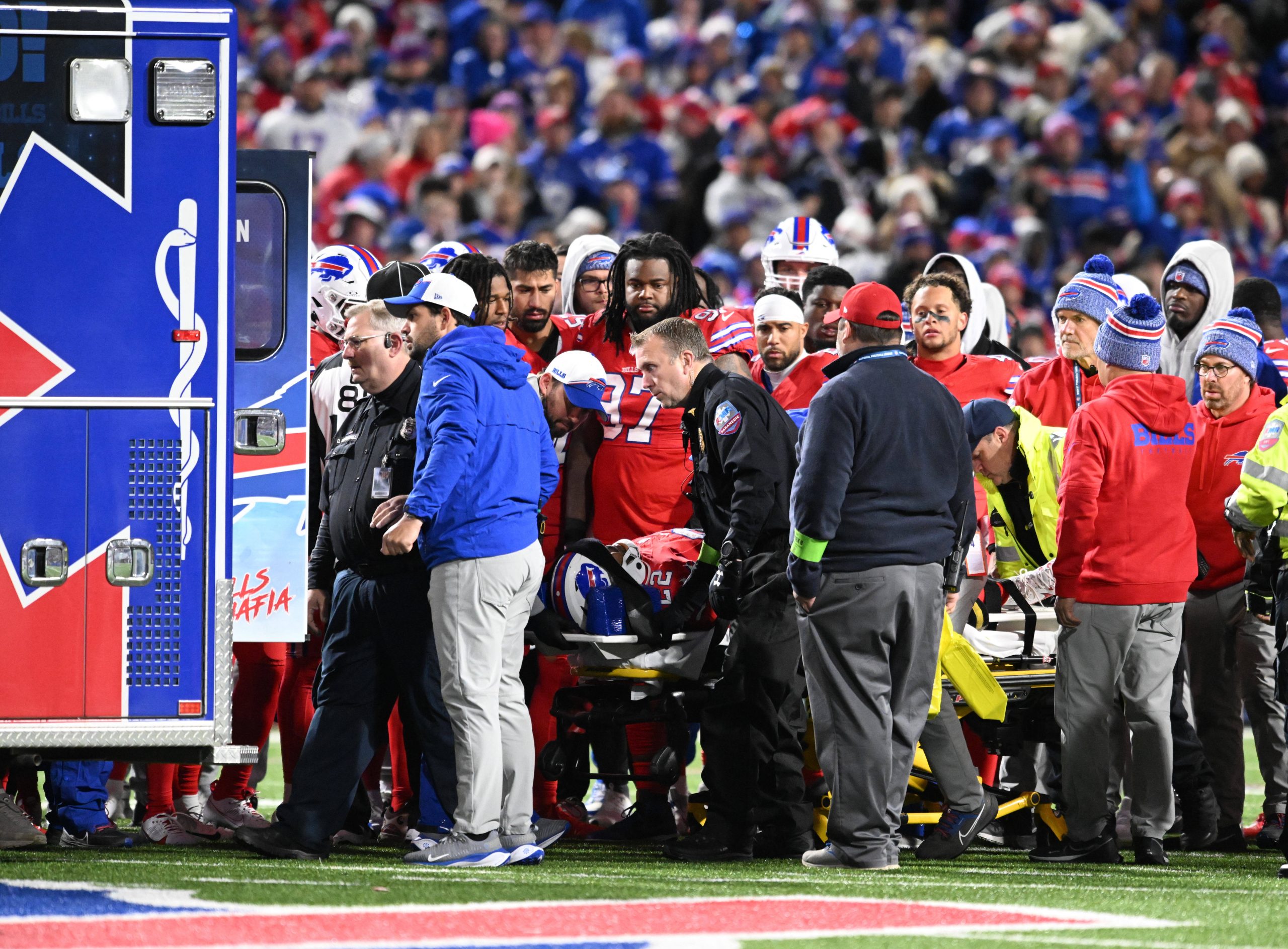 FootballR - NFL - Buffalo Bills RB Damien Harris aus dem Krankenhaus entlassen, während eine Gruppe von Menschen auf einem Footballfeld um einen Rettungswagen her