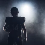 FootballR - NFL Game Pass 2024 - Die Silhouette eines Footballspielers, der einen Ball hält, vor einem dunklen Hintergrund, perfekt, um Ihr DAZN-Abo zu präsentieren.