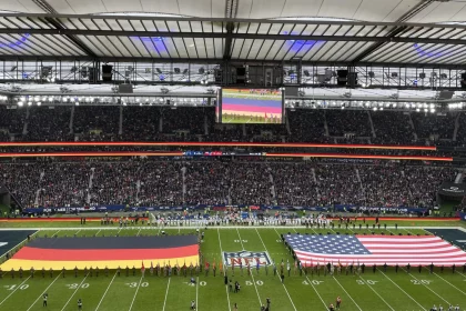 FootballR - NFL - Ein Stadion mit NFL-Spektakel mit amerikanischen und deutschen Flaggen auf dem Spielfeld. Viele Fußballstars und Prominente vor Ort.