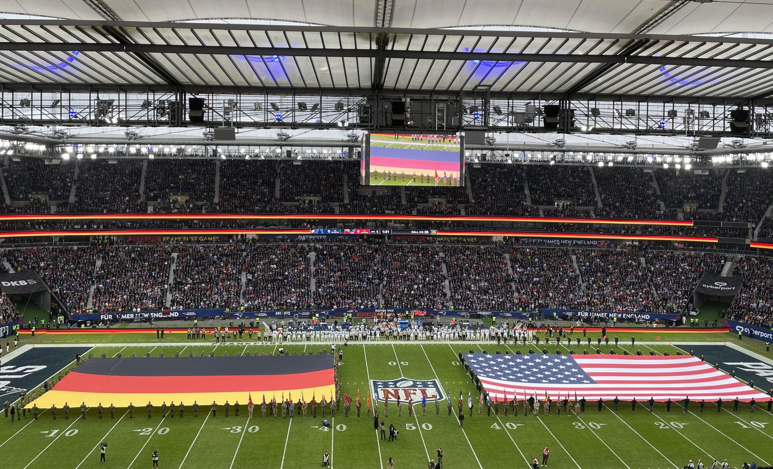 FootballR - NFL - Ein Stadion mit NFL-Spektakel mit amerikanischen und deutschen Flaggen auf dem Spielfeld. Viele Fußballstars und Prominente vor Ort.