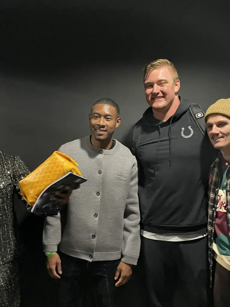 FootballR - NFL - Prominente Fußball-Stars David Alaba und Marcel Sabitzer posieren mit Colts Spieler Bernhard Raimann für ein Foto vor einer schwarzen Wand.