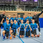 FootballR - NFL - Eine Gruppe von Kindern der Taufkirchner Schule posiert während des Deutschland-Finales der NFL FLAG Football für ein Foto auf einem Basketballplatz.