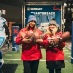 FootballR - NFL - Zwei Frauen halten während der Weihnachtszeit Fußbälle auf einer NFL-Bühne.