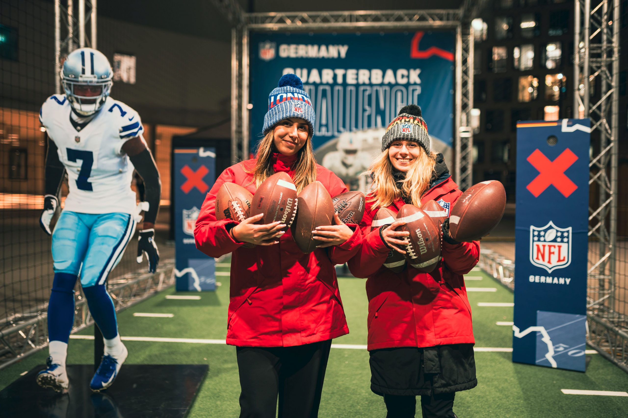 FootballR - NFL - Zwei Frauen halten während der Weihnachtszeit Fußbälle auf einer NFL-Bühne.