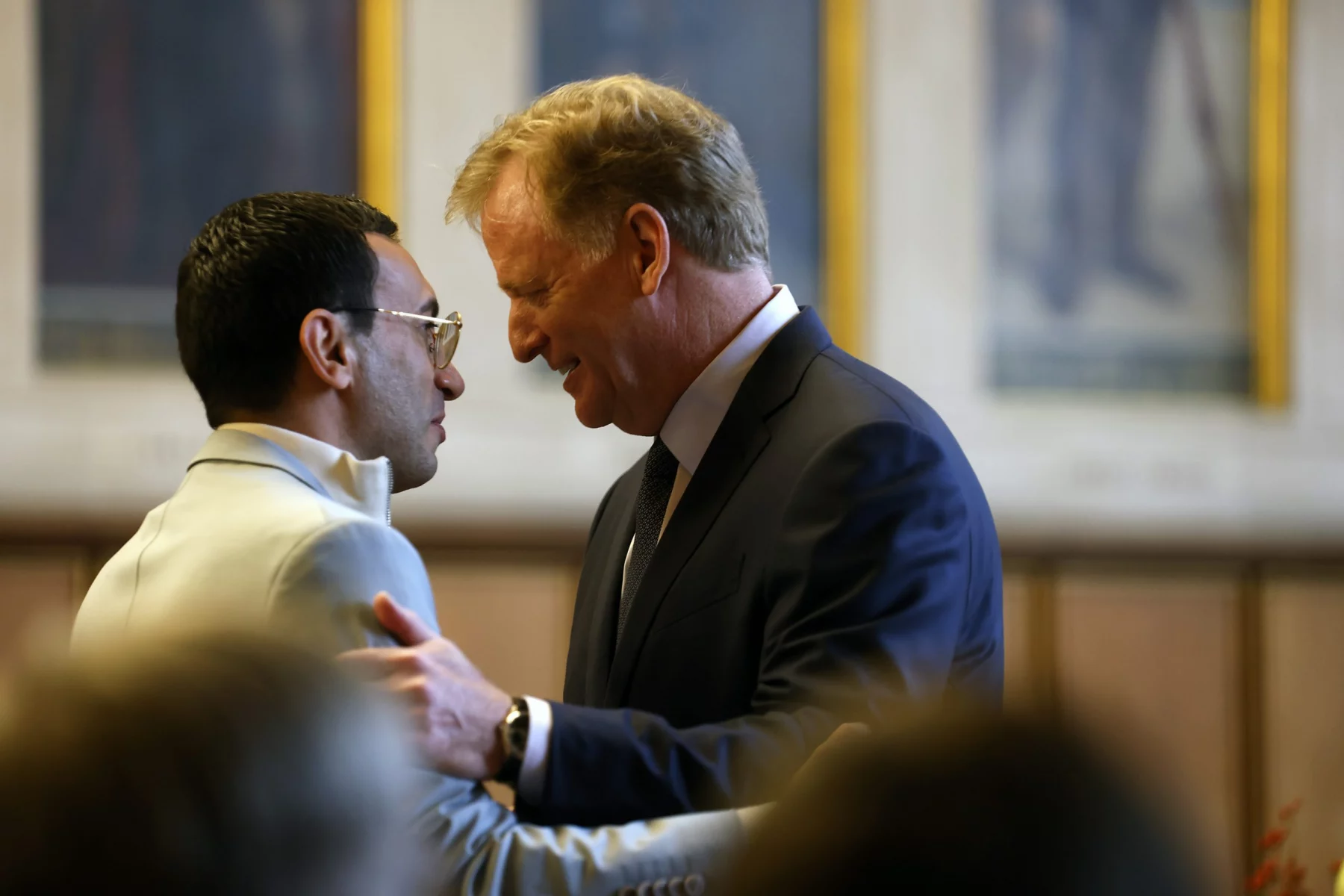 FootballR - NFL - Roger Goodell, der Commissioner der NFL, umarmt bei einer Veranstaltung in Frankfurt einen anderen Mann in Anzug und Krawatte.