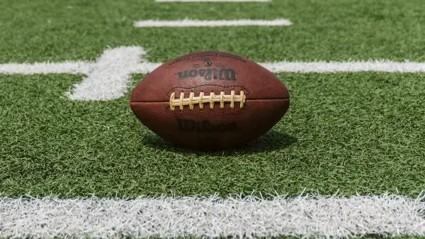 FootballR - NFL - Ein Football steht auf dem Feld eines Footballfeldes, während American-Football-Wetten und -Gemeinschaften inmitten der spürbaren Größenunterschiede gedeihen.