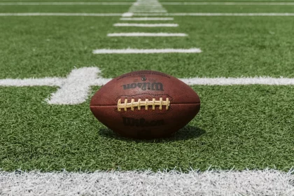 FootballR - NFL - Ein Football steht auf dem Feld eines Footballfeldes, während American-Football-Wetten und -Gemeinschaften inmitten der spürbaren Größenunterschiede gedeihen.