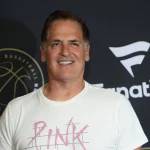 FootballR - NFL - NBA-Besitzer Mark Cuban, bekannt für seine aktive Präsenz in den sozialen Medien, posiert lässig auf einem schwarzen Teppich und trägt ein rosa T-Shirt.