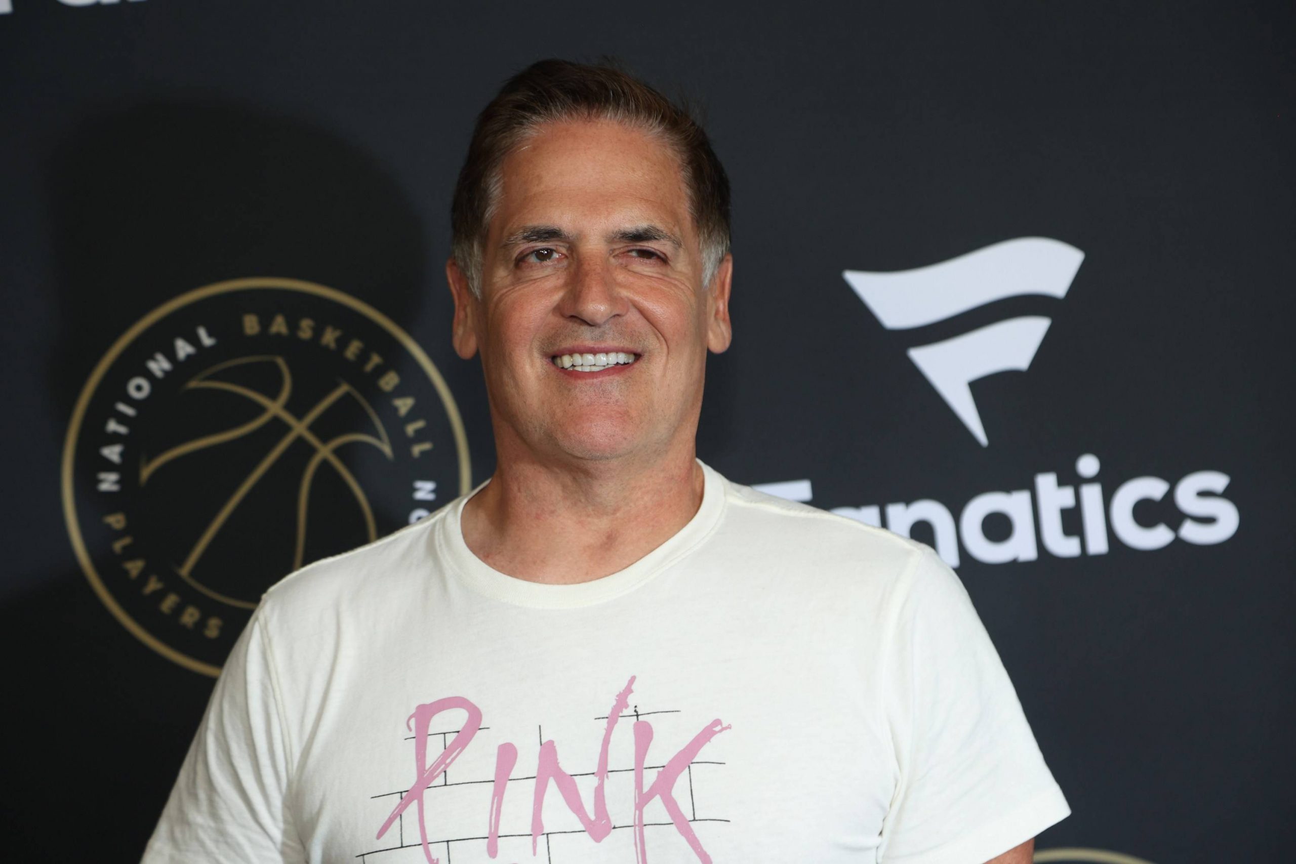 FootballR - NFL - NBA-Besitzer Mark Cuban, bekannt für seine aktive Präsenz in den sozialen Medien, posiert lässig auf einem schwarzen Teppich und trägt ein rosa T-Shirt.