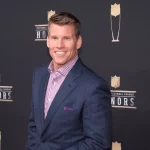 FootballR - NFL - Ein Mann im Anzug steht während einer Live-Übertragung auf einem roten Teppich im NFL RedZone Studio.