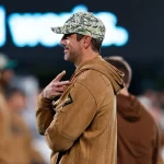 FootballR - NFL - Ein Footballspieler der New York Jets (aaron Rodgers) , der sich kürzlich eine Achillessehnenverletzung zugezogen hat, steht am Spielfeldrand und wartet sehnsüchtig auf seine Rückkehr ins Spiel.