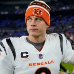 FootballR - NFL - Cincinnati Bengals Quarterback Joe Burrow in orange-weißer Uniform steht auf einem Feld.