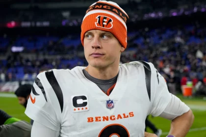 FootballR - NFL - Cincinnati Bengals Quarterback Joe Burrow in orange-weißer Uniform steht auf einem Feld.